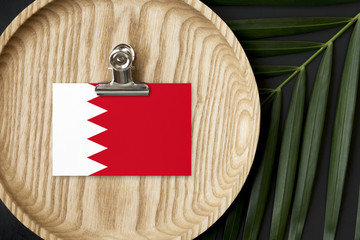 Bahrain flag tagged on wooden plate. Tropical palm leaves monstera on background. Minimal national...