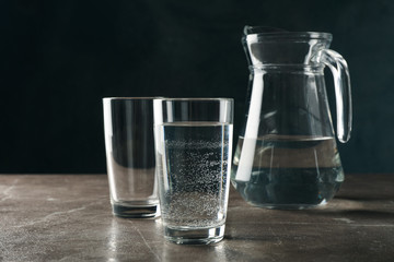 Jug with water and glasses on gray table, space for text