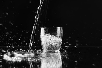 Pouring purified fresh water in glass on mirror background