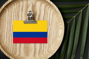 Colombia flag tagged on wooden plate. Tropical palm leaves monstera on background. Minimal national concept.