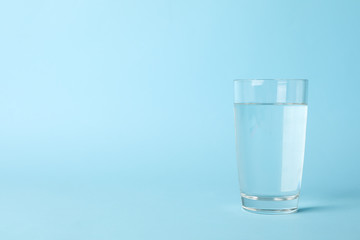 Glass of water on blue background, space for text