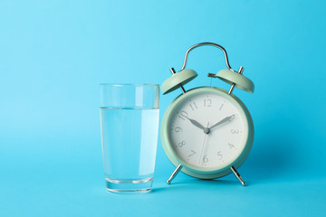 Alarm clock and glass of water on blue background, close up