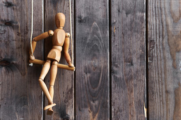 a wooden model of a man hangs on ropes like a marionette on a brown wooden background