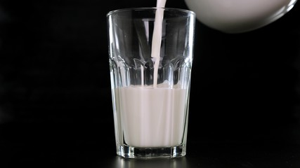 Milk is poured into a glass black background. Close up.