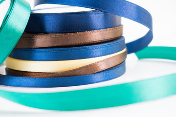 Stack of satin ribbon coils. Blue, green, brown and yellow ribbon for handmade. Needlework items.