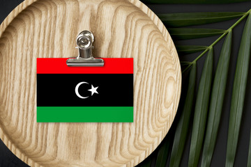Libya flag tagged on wooden plate. Tropical palm leaves monstera on background. Minimal national...