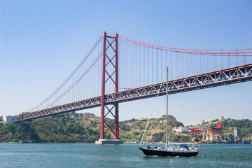 sailing yacht passing the Bridge of the 25 th of April, over the river Tejo in Lisbon, Portugal