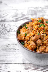 Pilaf with meat in a ceramic bowl on the white wooden table. Traditional oriental cuisine meal
