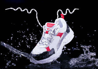Sports sneakers on a black isolated background in splashes of water, youth sports shoes, floating laces in the air