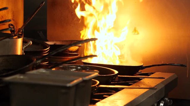 Big flame on the pan. A lot of kitchenware. Dangerous fire in the kitchen. There are metal bowls and pans a well.