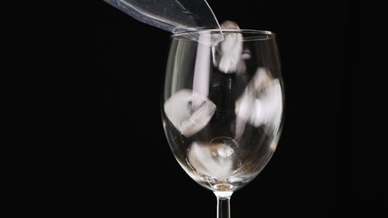 Pour ice cubes into a glass on black background. Close up.