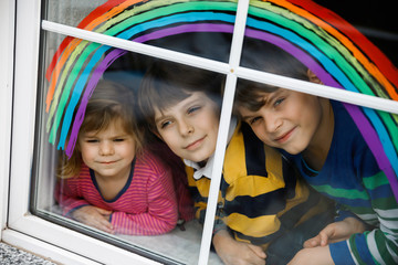 Three kids, two school kids boys and toddler girl with rainbow painted with colorful window color...