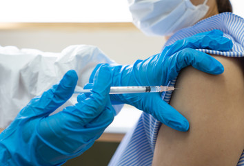 A doctor wearing gloves is injecting the vaccine to the woman patient in the hospital. covid-19,...