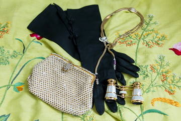 Flat lay opera themed photo of vintage pearled evening bag, long black gloves, necklace and mother...