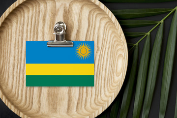 Rwanda flag tagged on wooden plate. Tropical palm leaves monstera on background. Minimal national concept.