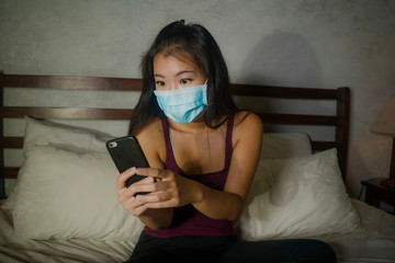 young beautiful scared and overwhelmed Asian Korean woman in protective mask checking online news worried about coronavirus pandemic