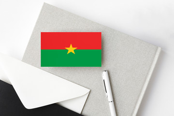 Burkina Faso flag on minimalist letter background. National invitation envelope with white pen and notebook. Communication concept.