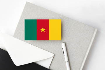 Cameroon flag on minimalist letter background. National invitation envelope with white pen and notebook. Communication concept.