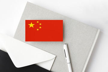 China flag on minimalist letter background. National invitation envelope with white pen and notebook. Communication concept.