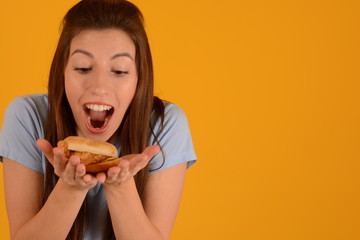 joyful woman looks at a burger with meat on a yellow background fast food