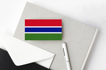 Gambia flag on minimalist letter background. National invitation envelope with white pen and notebook. Communication concept.
