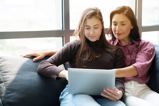 Mother and daughter sit play tablet on the sofa Family doing activities at home on weekends in the living room. Watch movies, listen to music, learn languages and shop online. Concept families at home - Powered by Adobe