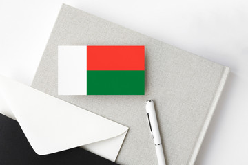 Madagascar flag on minimalist letter background. National invitation envelope with white pen and notebook. Communication concept.