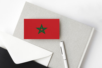 Morocco flag on minimalist letter background. National invitation envelope with white pen and notebook. Communication concept.
