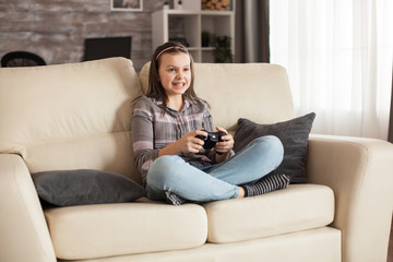 Little girl with braces sits on sofa playing video games