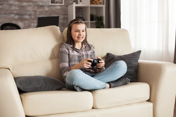 Obraz premium Little girl with braces sits on sofa playing video games