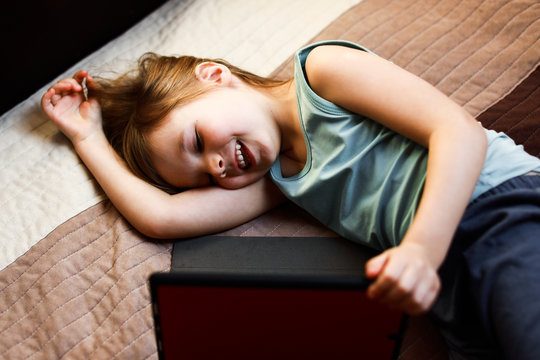 todder girl laying on the bed looking at the tablet and smiling