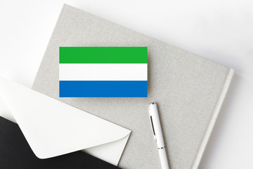 Sierra Leone flag on minimalist letter background. National invitation envelope with white pen and notebook. Communication concept.