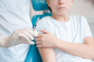 Woman doing injection to teen boy, selective focus. Female doctor with vaccine shot in hand. Healthcare concept. Nurse with syringe. Teenager in clinic.