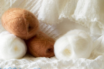 Photo illustration on the topic of knitting. Delicate white and brown yarn is located on the background of a white knitted fabric.