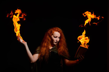 An ominous witch with long curly hair holds a magical fire. Tongues of flame on the palms of a...