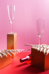 Bottle of pink rose wine and flutes, golden branches and geometrical boxes. Celebration, aperitif concept