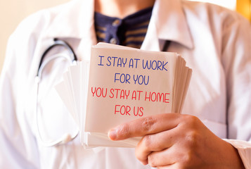 doctor holding paper with message, I STAY AT WORK FOR YOU, YOU STAY AT HOME FOR US
