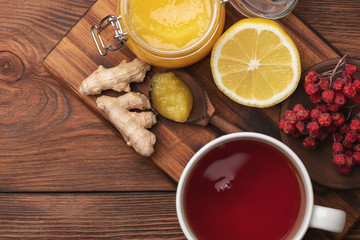 Fototapeta na wymiar Hot tea, lemon, ginger roots and honey on dark wooden plate. Alternative medicine still life close up.