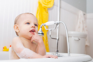 Portrait of cute baby boy sitting in bathtub biting finger