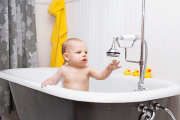 Curious baby boy sitting in bathtub touching dropping water