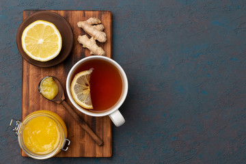 Obraz na płótnie Canvas flat lay of natural ingredients for tea to increase immuntiy during self-isolation period. lemon on a wooden plate, ginger, hot tea and honey in a wooden spoon.