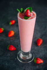 A tall glass with pink drinks or beverages from juicy and fresh red strawberries
