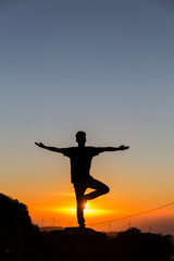 backlight of a man doing yoga while watching a sunset on a clear day