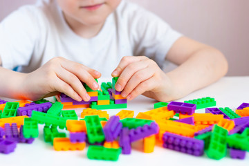 A child plays with a bright constructor on a white table. The development of fine motor skills of the hands. Quarantined home leisure.