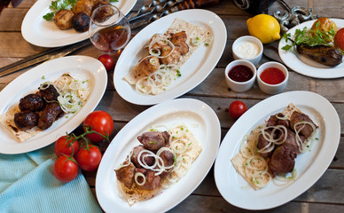 Assorted barbecue meat is served on white plates on a wooden background with sauces and vegetables. Gala dinner