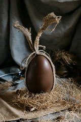 Brown Easter sweet chocolate egg in burlap bag on gray background