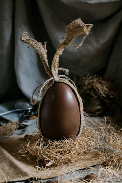 Brown Easter Sweet Chocolate Egg In Burlap Bag On Gray Background