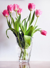 Pink tulips in a transparent vase on a table near a light wall