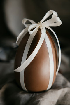 Delicious seasonal chocolate Easter egg with a ribbon on a gray background