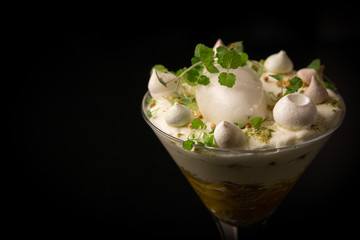 Mango dessert with lemon sorbet, cream, small merengue and mint in a martini glass on a black background. 